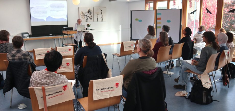 Erwachsene sitzen in einem Raum und schauen auf eine Leinwand.