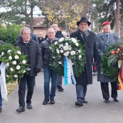 Männer auf einem Friedhofsweg, die drei Trauerkränze tragen