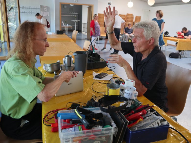 Zwei Männer unterhalten sich an einem Tisch mit elektrischen Geräten