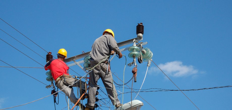 Weitwinkelaufnahme von Leitungsarbeitern, die an einem Hochspannungsmast arbeiten