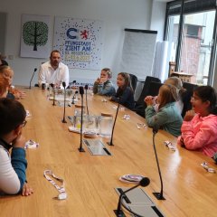 Kinder sitzen mit Bürgermeister am großen Tisch im Magistratszimmer