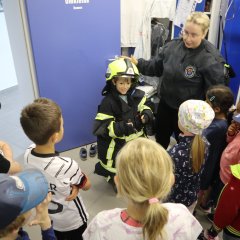 Feuerwehrfrau erklärt Kindern eine Feuerwehrausrüstung 