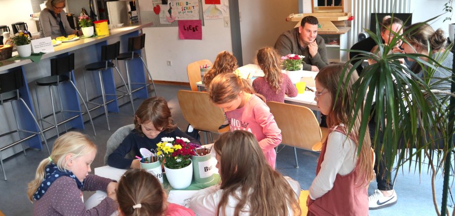 Kinder und Eltern sitzen an Tischen, malen und essen Kuchen